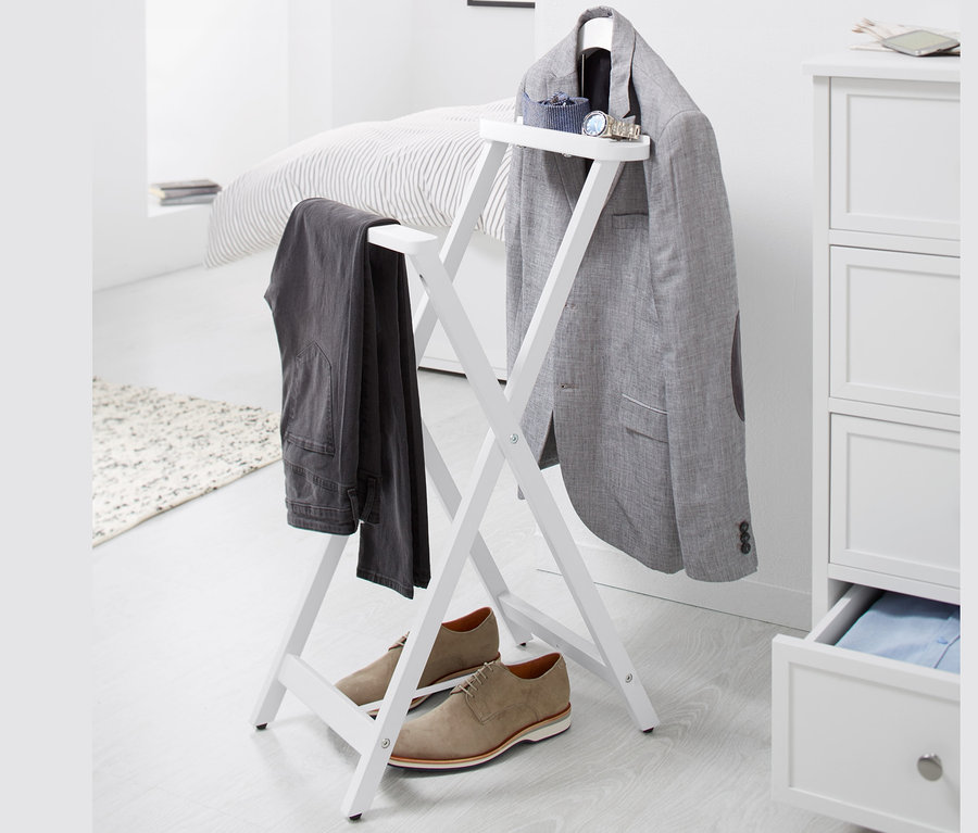 Na białym tle stoi składany wieszak typu lokaj na ubrania, na którym wisi szary blezer i spodnie, a pod nim stoją brązowe buty.